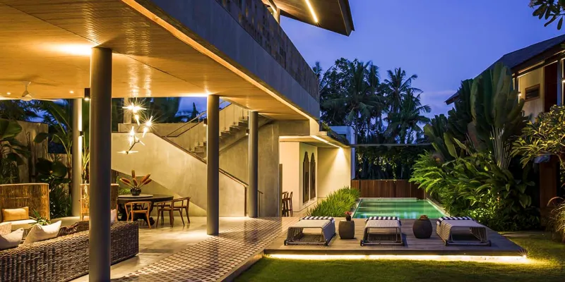 Modern villa exterior at dusk with illuminated pool and lush garden at caSabama