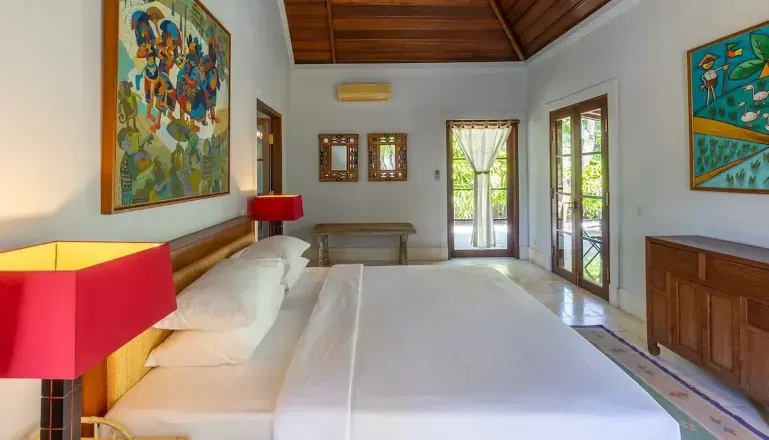 Cozy bungalow bedroom featuring a large bed, traditional thatched roof, and rustic wooden furniture at Villa Angsa