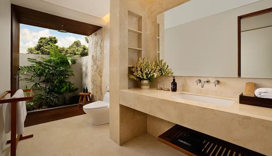 Bright marble bathroom featuring a wide vanity, large mirror, and open air shower with lush tropical plants at Amarta Beach Retreat 2BR Villa