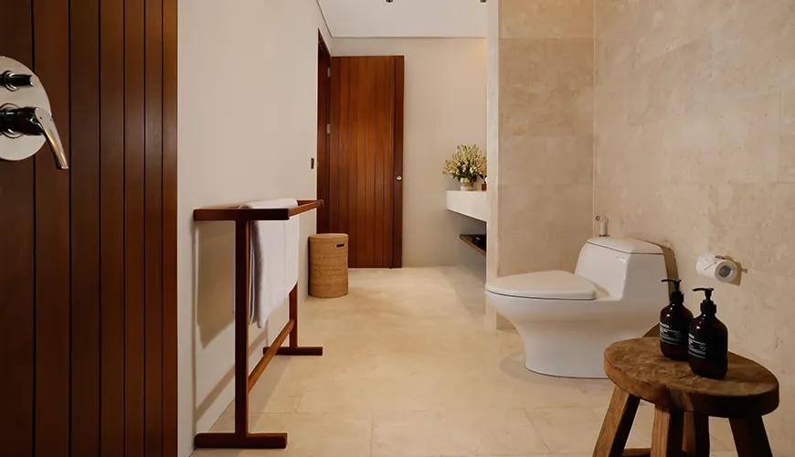 Clean bright villa bathroom featuring natural stone flooring, marble accent wall, and modern wooden towel rack at Amarta Beach Retreat 2BR Villa
