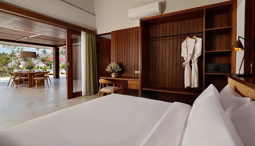 Second bedroom with crisp white bedding, beautiful wood furnishings, and direct access to the villa dining area at Amarta Beach Retreat 2BR Villa