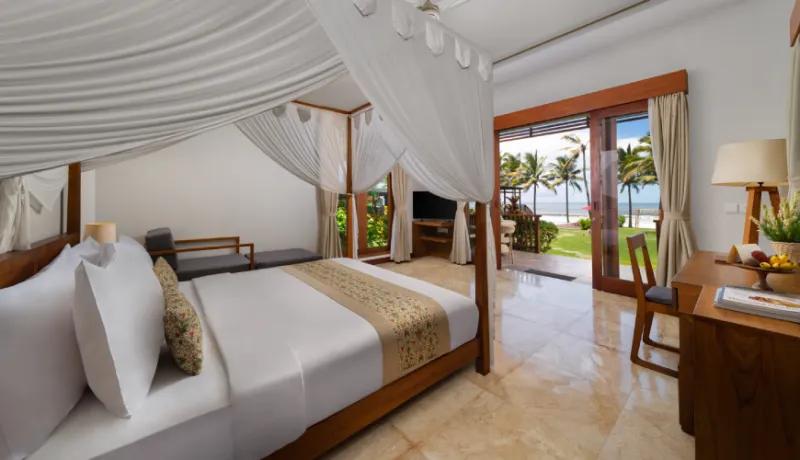 Luxurious resort suite with a wooden four poster bed and terrace overlooking the tropical coast at Amarta Beach Retreat