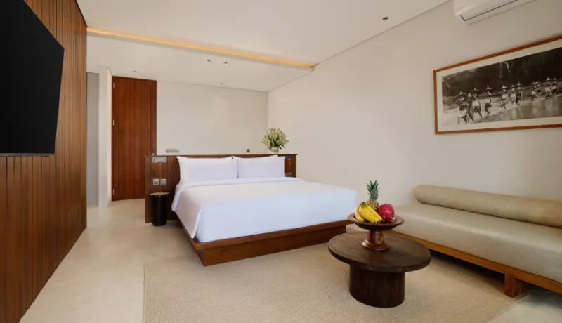 Minimalist bedroom featuring a white bed and a wooden accent wall overlooking a green garden at Amarta Beach Retreat