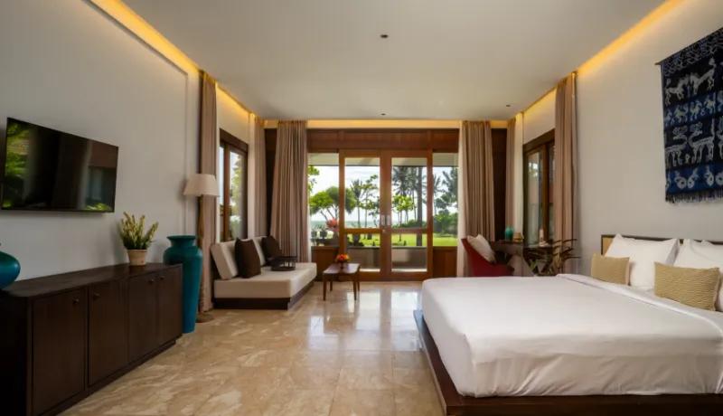Modern naturalist bedroom with polished stone tile and wooden furniture facing a bright tropical ocean horizon at Amarta Beach Retreat