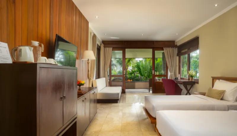 Spacious naturalist bedroom with twin beds and dark wood cabinets overlooking a lush tropical garden at Amarta Beach Retreat