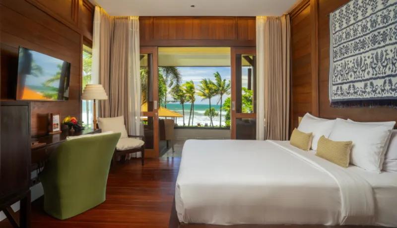 Warm wood lined bedroom with a soft white bed and expansive sliding doors overlooking the beachfront at Amarta Beach Retreat