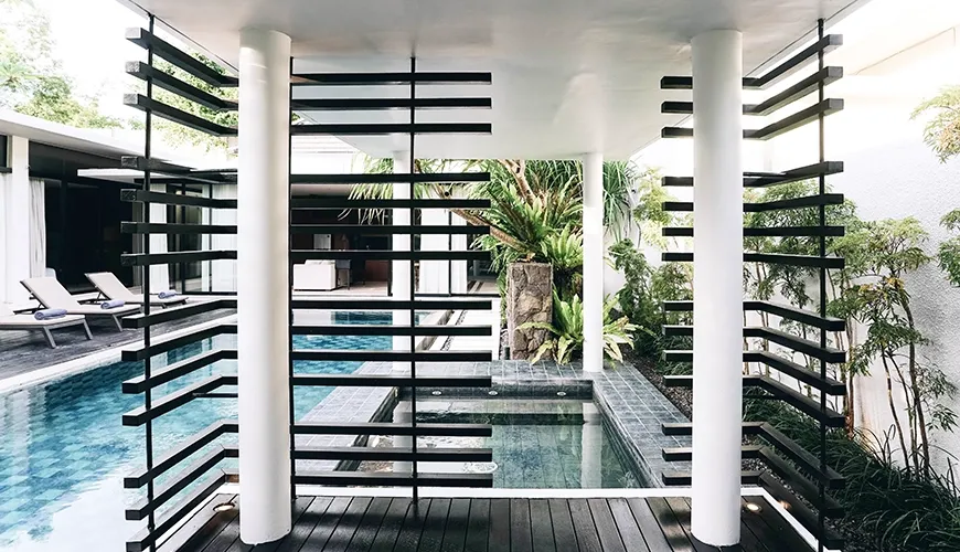 Contemporary covered poolside gazebo with white columns and dark wooden slats providing shade for the adjacent mini spa pool, connected to the main swimming pool area at Ambergris Villa