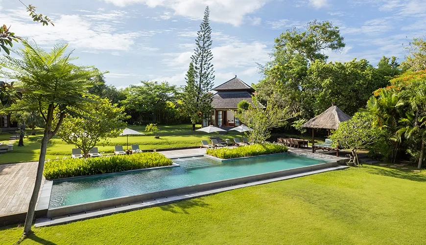 Large outdoor swimming pool surrounded by a vast green lawn and tropical landscape at Amita Villa
