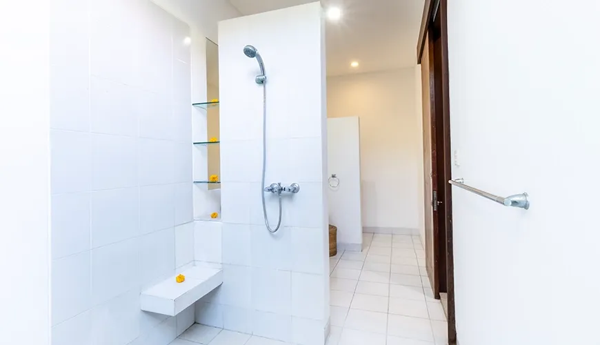 Brightly lit guest bathroom shower stall featuring crisp white tiles, a handheld fixture, recessed glass shelves, and a seat at Asraya Villa