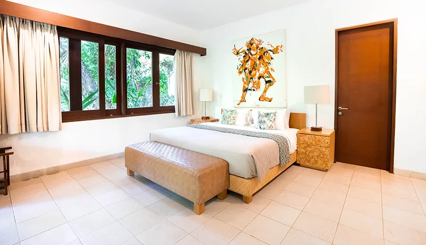 Chic villa bedroom featuring a queen-sized bed, unique contemporary artwork, large windows, and a comfortable leather bench at Asraya Villa