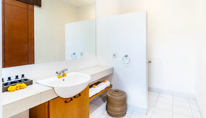 Clean white villa guest bathroom with a modern vessel sink, large mirror, and open wood shelving for towels at Asraya Villa