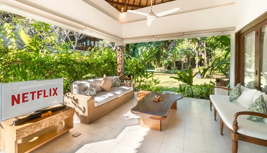 Inviting covered villa terrace featuring comfortable outdoor seating, a television, and beautiful views of the tropical garden lawn at Asraya Villa