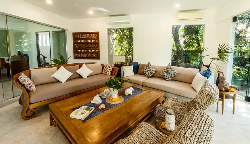 Inviting villa living room with custom carved wooden sofas, comfortable cushions, and large windows offering garden views at Asraya Villa