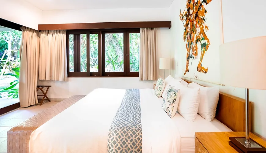 Modern villa bedroom featuring a large bed, dramatic abstract artwork, wood framed windows, and direct garden access at Asraya Villa