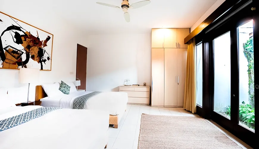 Modern villa guest suite with separate twin beds, built-in wardrobe, and direct access to a private outdoor garden area at Asraya Villa