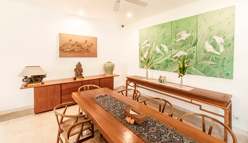 Spacious tropical villa dining area showcasing traditional furniture, unique artwork, a console table, and a cooling ceiling fan at Asraya Villa