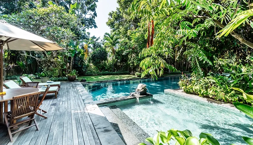 Stunning private villa pool area with a wooden deck, comfortable sun loungers, and lush tropical foliage for relaxation at Asraya Villa