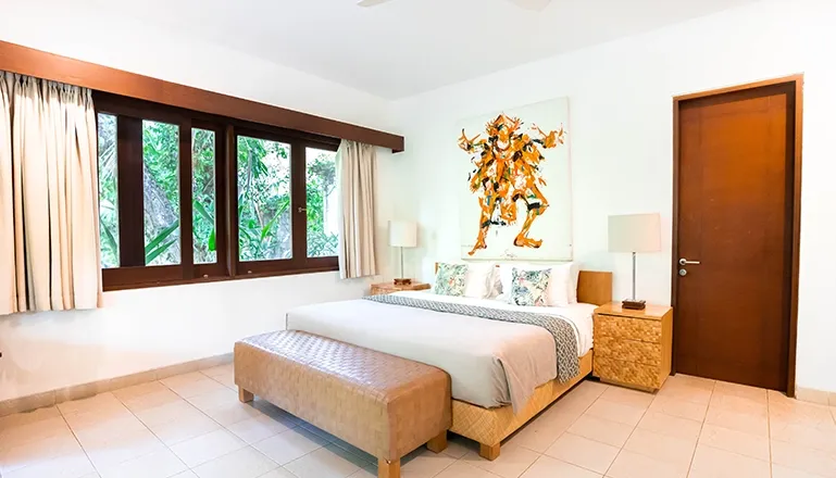 Sunny bedroom showcases a cozy bed a wide window and impressive wall art at Asraya Villa