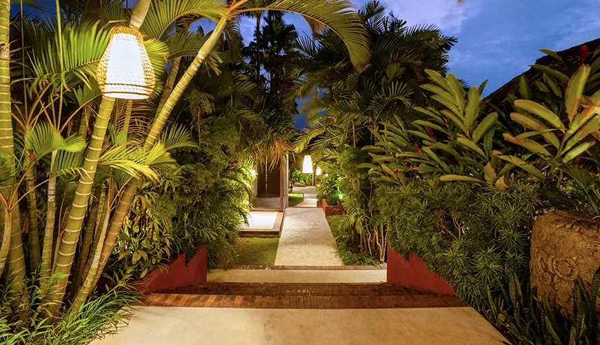 Tropical garden pathway illuminated hanging lights green foliage evening sky entrance at Bumbak Park
