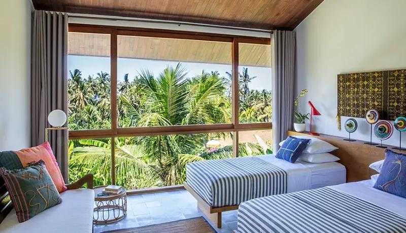 Luxury twin bed villa room featuring striped bedding and large window overlooking lush tropical palm trees at Casabama
