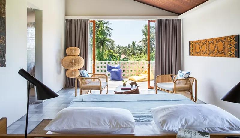 Modern bedroom villa with king size bed rattan lounge chairs and lush tropical garden views at Casabama