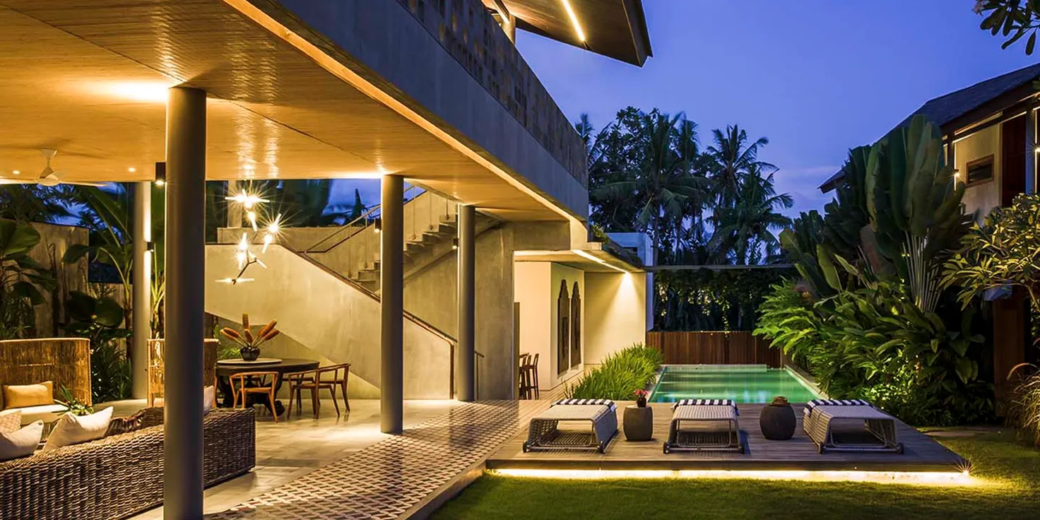 Modern villa exterior at dusk with illuminated pool and lush garden at caSabama