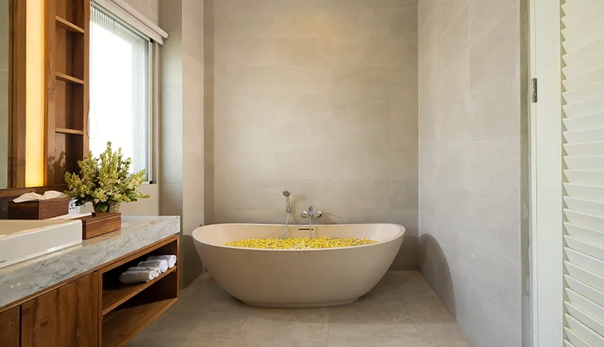 Spacious master bedroom bathroom featuring a modern free standing bathtub with yellow flowers floating in the water at Christie Villa