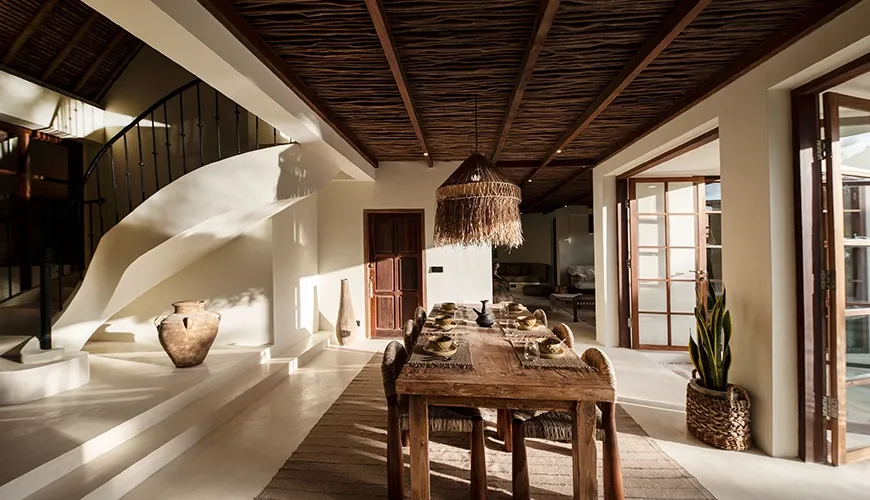Elegant luxury villa dining room featuring a large rustic wooden table under a textured woven timber ceiling and a curved staircase at Villa Xanadu