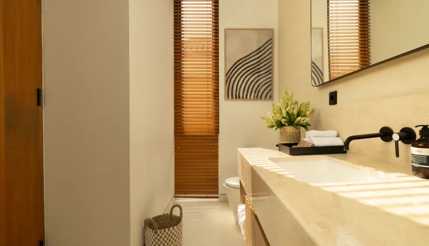 Sunny minimalist bathroom with travertine sink and wooden blinds at Fenta Villa