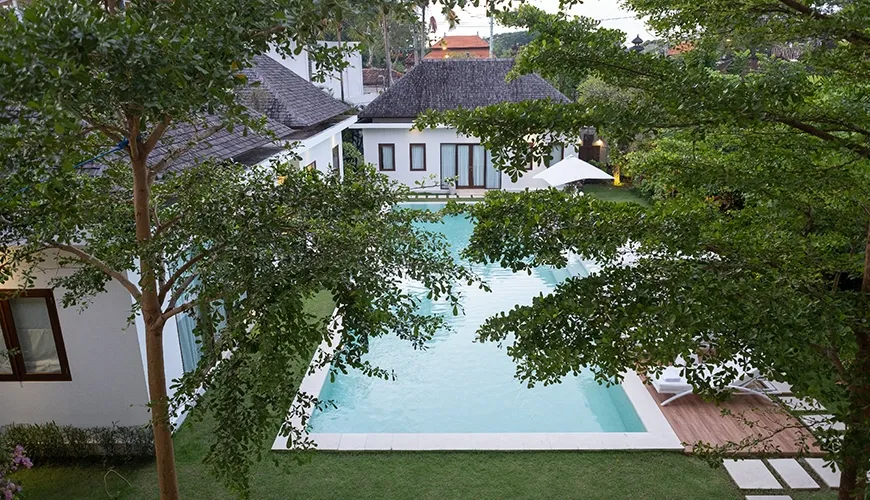 Elevated view of a luxurious rectangular swimming pool surrounded by a green lawn and secluded tropical garden at Istana Putih Villa