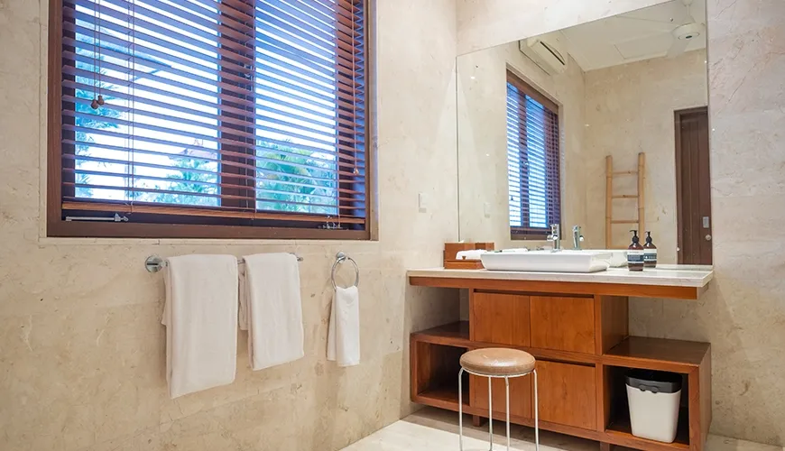 Modern villa bathroom with beige marble walls, wooden vanity, rectangular vessel sink, and large mirror at Istana Putih Villa