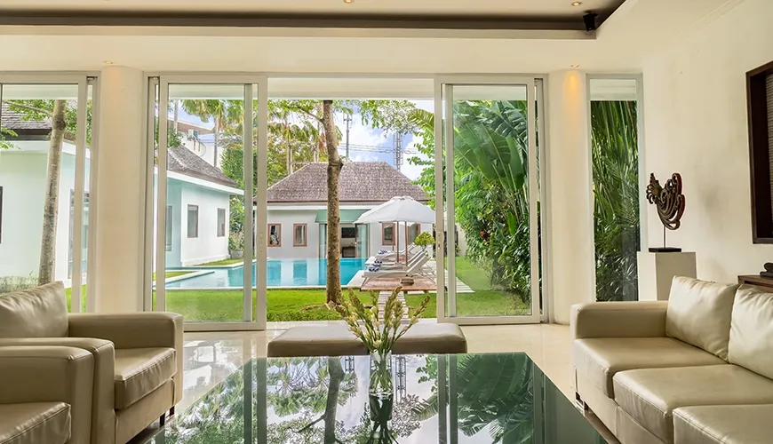 Modern villa living area with leather sofas, glass table, and wide sliding doors opening to the private pool at Istana Putih Villa