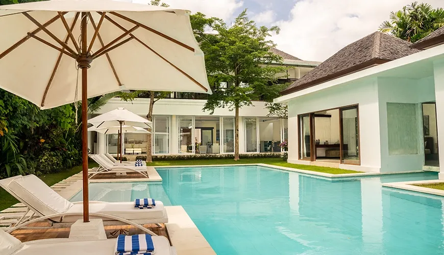 Resort-style swimming pool with elegant sun beds and shade umbrellas on a sunny day at Istana Putih Villa
