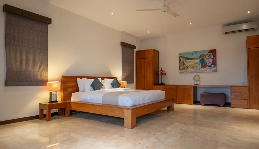 Spacious contemporary villa bedroom with wooden furniture, slatted headboard, colorful artwork, and polished marble floor at Istana Putih Villa