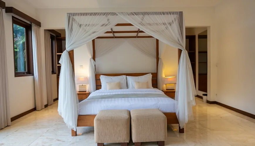 Tranquil villa bedroom with a wooden four-poster bed, sheer white netting, and elegant polished marble floor at Istana Putih Villa
