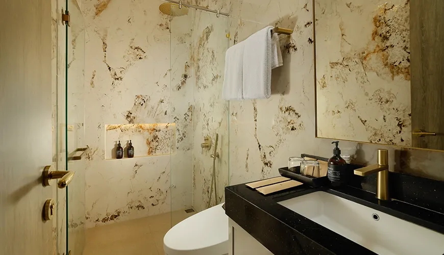 Luxurious bathroom with elegant marble walls, a spacious walk-in shower, and a modern sink at Kalem Uluwatu