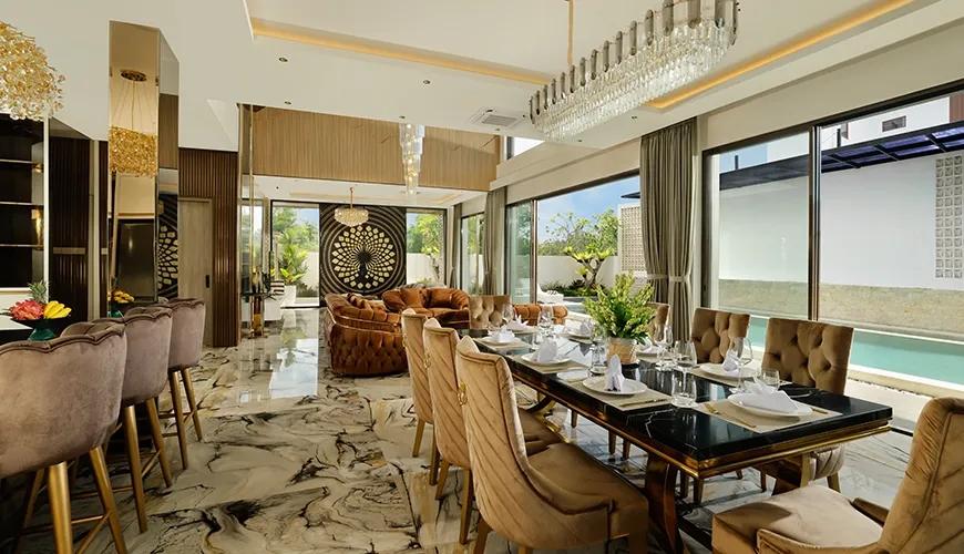 Open plan villa interior featuring an elegant dining table and lounge area overlooking a blue pool at Kalem Uluwatu