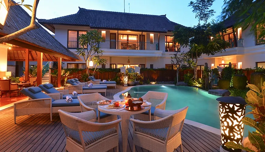 A beautiful pool area at dusk with a sunset theme and romantic dining table at Kama Village 1BR
