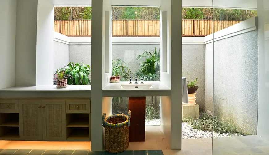 A luxurious semi-indoor bathroom featuring a modern sink a glass shower and a private garden view at Kama Village 1BR