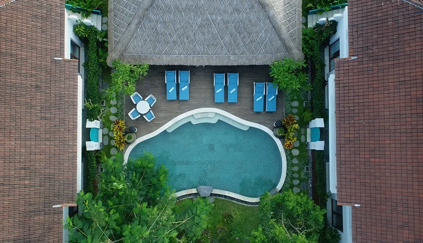 An aerial view of a tropical villa resort featuring a large swimming pool and sunbeds surrounded by lush greenery at Kama Village 1BR