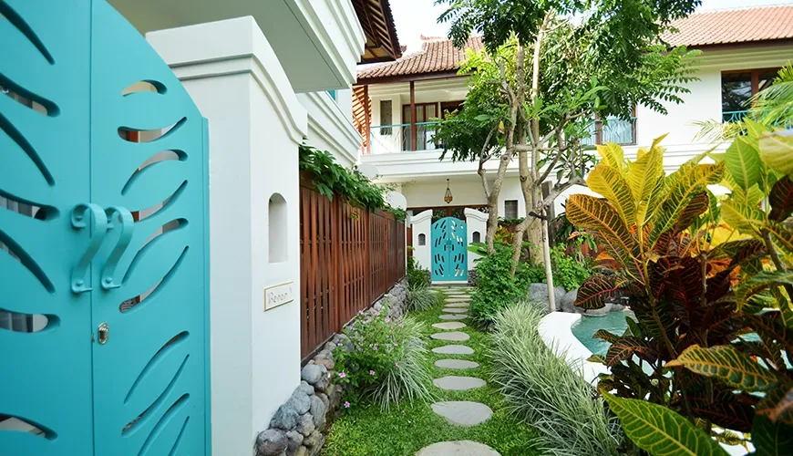 Beautiful garden hallway with a white and blue theme and a stone path surrounded by lush tropical greenery at Kama Village 1BR