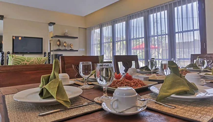 Elegant dining table set for guests with folded green napkins, polished glassware, and delicious prepared food plates at Kumuda Villa