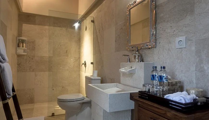 Elegant full bathroom with toilet, glass shower stall, and a small dark wood cabinet for toiletries and essentials at Kumuda Villa