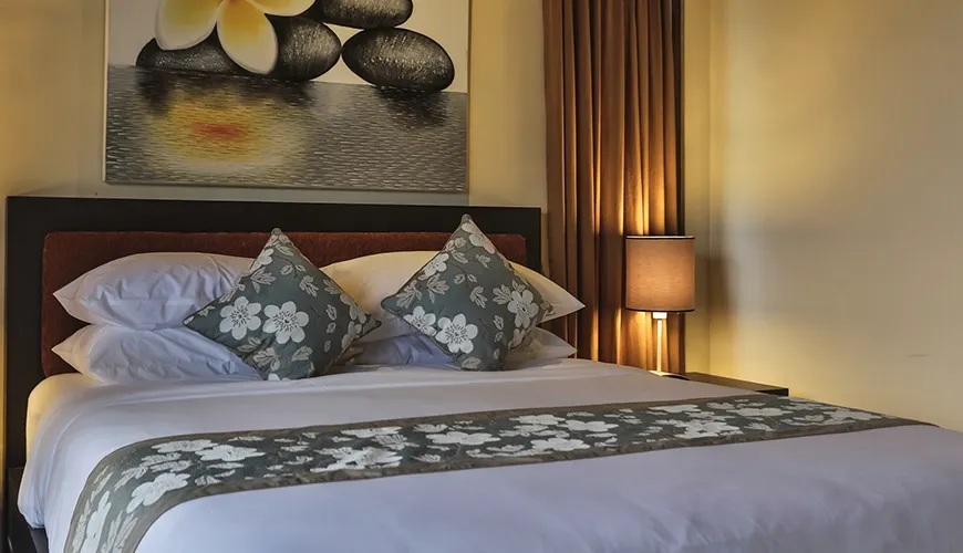 Inviting bedroom featuring dark wood headboard, elegant patterned bed runner, and decorative pillows with floral embroidery at Kumuda Villa