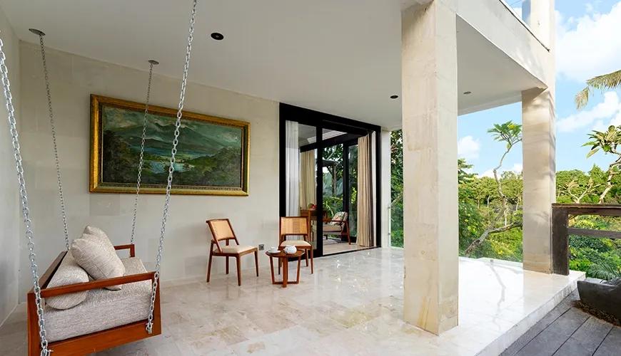 Bright open Maharani Balcony area with stone flooring, featuring a wooden swing sofa and sweeping forest views at Le Sunset