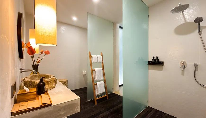 Contemporary family bathroom featuring a stone vessel sink, frosted glass shower panels, and dark wood flooring at Le Sunset