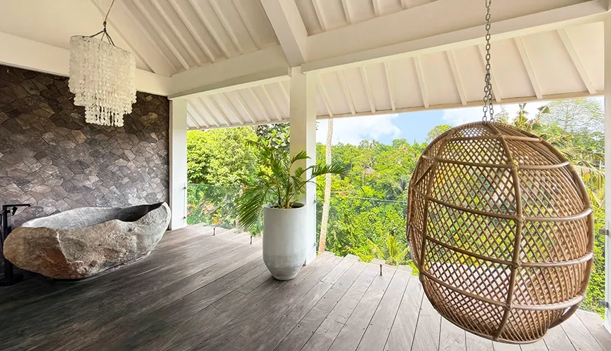 Exotic master bathroom balcony featuring a carved stone bathtub and a comfortable woven hanging chair at Le Sunset Villa