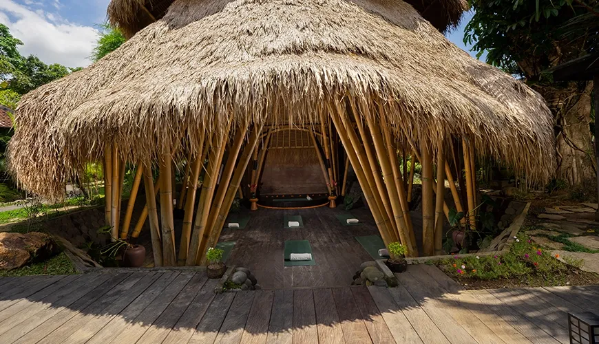 Open air bamboo yoga shala structure with a thatched roof and mats laid out on a wooden deck at Le Sunset Villa