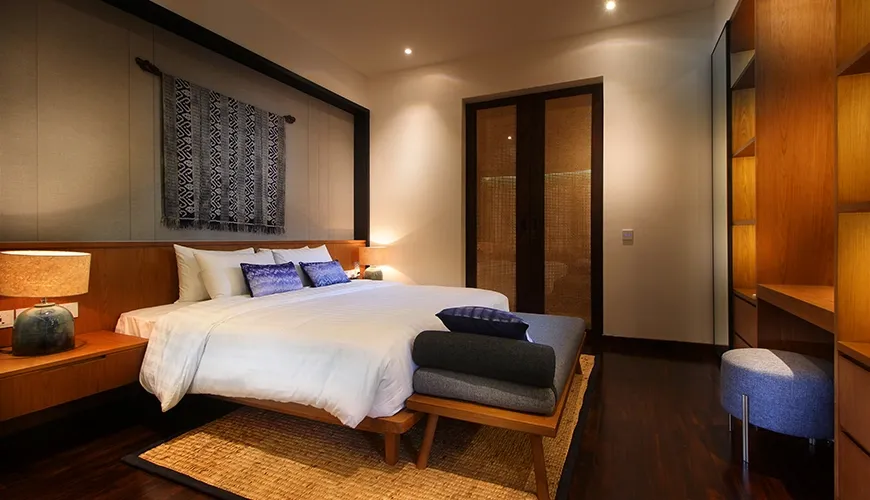 Contemporary bedroom design contrasts bright white bedding with rich dark wood paneling, featuring striking woven wall art at Leceni Villa