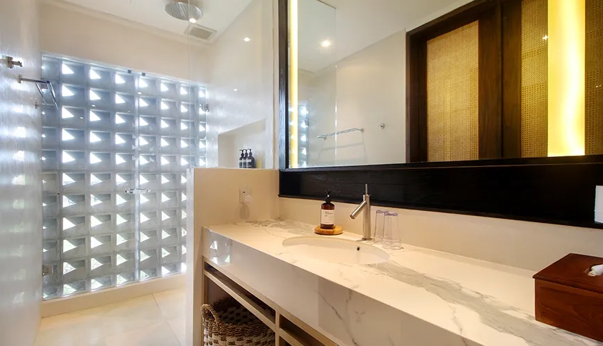 Modern luxury bathroom vanity area with warm strip lighting around a mirror and rain shower visible at Leceni Villa